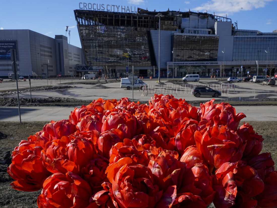 A bouquet of flowers inserted into the road fence in front of the burnt Crocus City Hall (center) on the western outskirts of Moscow, on March 27, after an attack by ISIS-K killed 145 people and inured hundreds more.