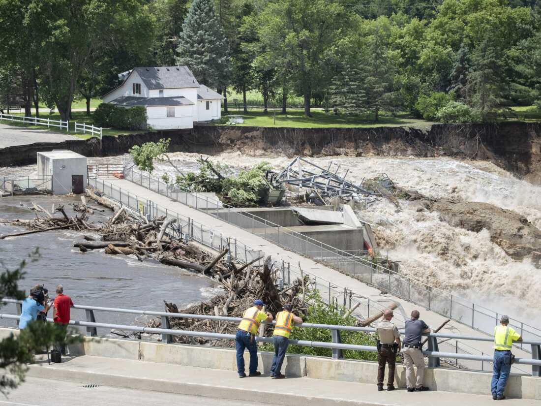 Onlookers take in the catastrophic damage to the Rapidan Dam site in Rapidan, Minn., on Monday. Debris blocked the dam, forcing the heavily backed up waters of the Blue Earth River to reroute along the bank nearest the Dam Store.