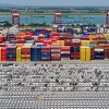Chinese-made cars are lined up in rows at the port in Nanjing, China. Behind the cars are stacks of cargo shipping containers in a variety of colors — blue, red, yellow, brown, orange.