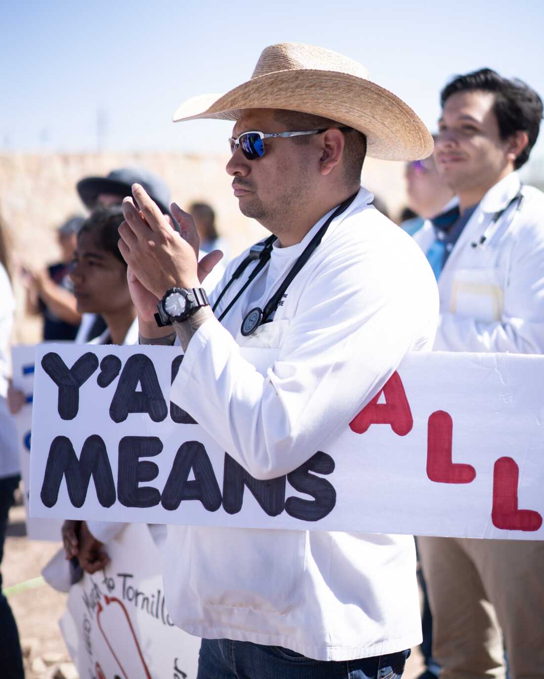 "Y'all means all" has emerged as a slogan of support for immigrants and other marginalized communities. In this 2018 photo, Ricardo Gámez of El Paso holds a sign bearing the words at the Tornillo Port of Entry in Tornillo, Texas, as medical professionals called for quick reunification of some 2,700 migrant children with their families.