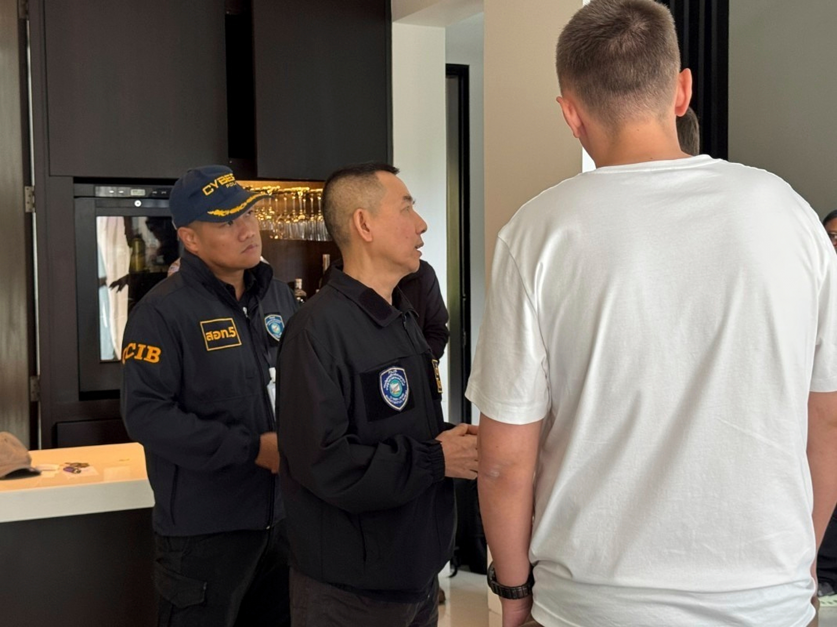 A 35-year-old suspected Russian hacker, identified in Russian media as Denis Obrezko, right, back to camera, with cyber police after he was arrested in Phuket, Thailand on Nov. 6. 2025. (Thailand