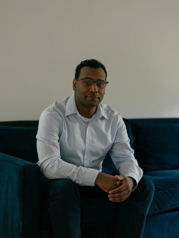 Ian Moss is a former official at the U.S. Department of State who helped coordinate the grandsons' travel to the United States. He poses for a portrait, looking at the camera while sitting on a couch.