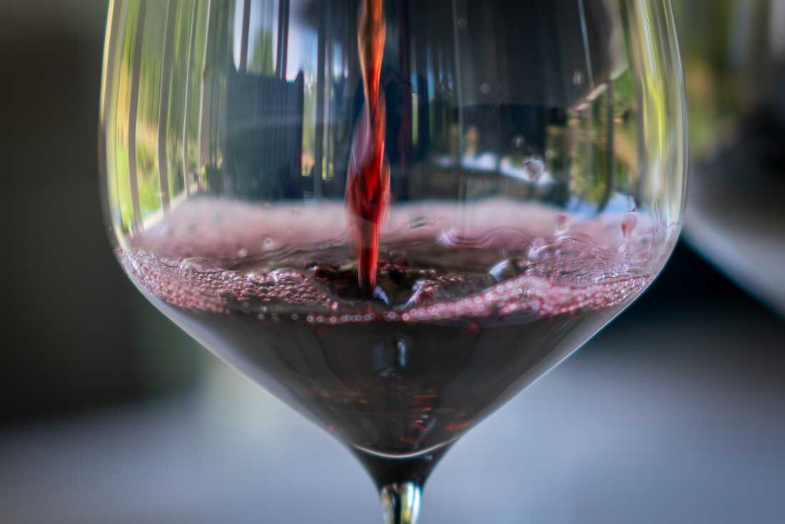 This photo shows a close-up of red wine pouring into a wine glass.