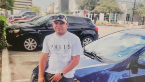 A man sits on the hood of a blue car while look at the camera.