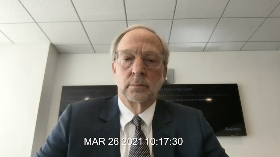 This screenshot shows Rick Jacobs from roughly the shoulders up, testifying at his videotaped deposition. He's wearing a dark suit, a white shirt, a tie and glasses. This screenshot shows Rick Jacobs from roughly the shoulders up, testifying at his videotaped deposition. He's wearing a dark suit, a white shirt, a tie and glasses.