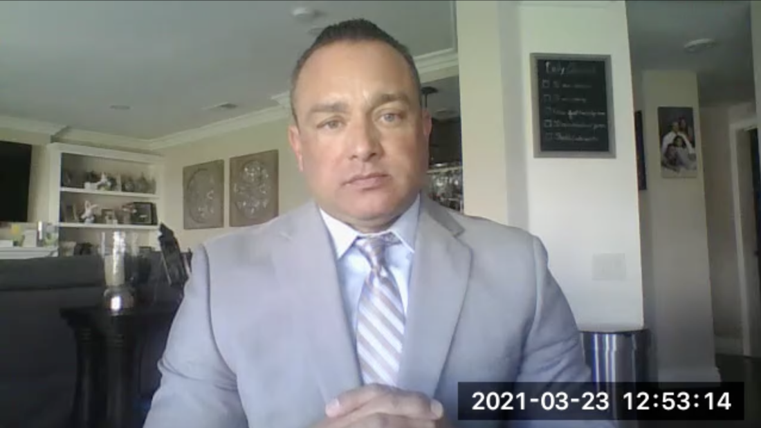 This screenshot shows LAPD officer Matthew Garza from the elbows up, testifying against Rick Jacobs. He's wearing a gray suit jacket, a striped tie and a white shirt. This screenshot shows LAPD officer Matthew Garza from the elbows up, testifying against Rick Jacobs. He's wearing a gray suit jacket, a striped tie and a white shirt.