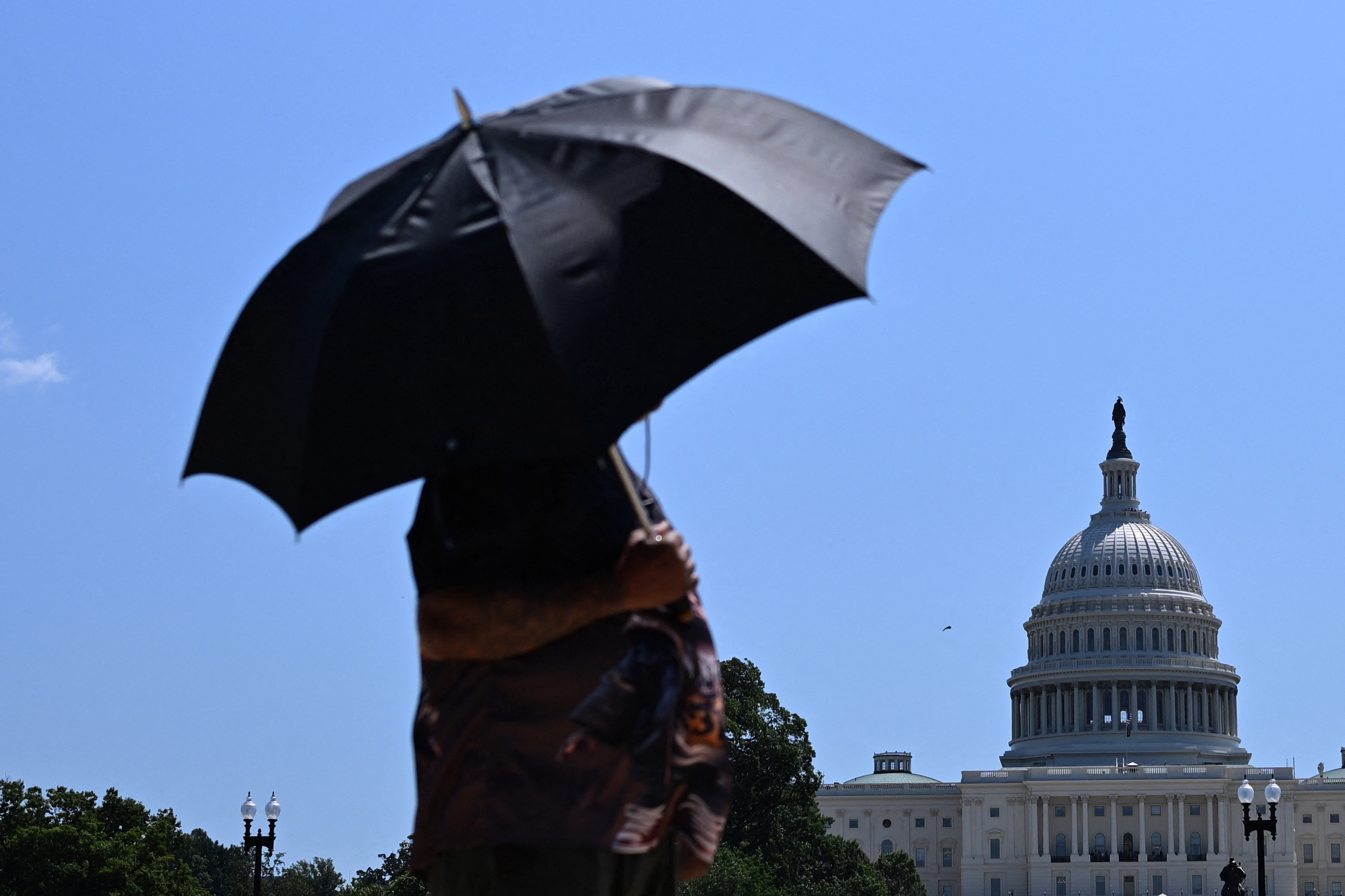 A person uses an umbrella as they walk near Capitol Hill in Washington, D.C., on Friday. The United States is experiencing its first significant heat wave of the year, across the Great Plains and expanding into parts of the Midwest and Great Lakes over the weekend, according to the National Weather Service.