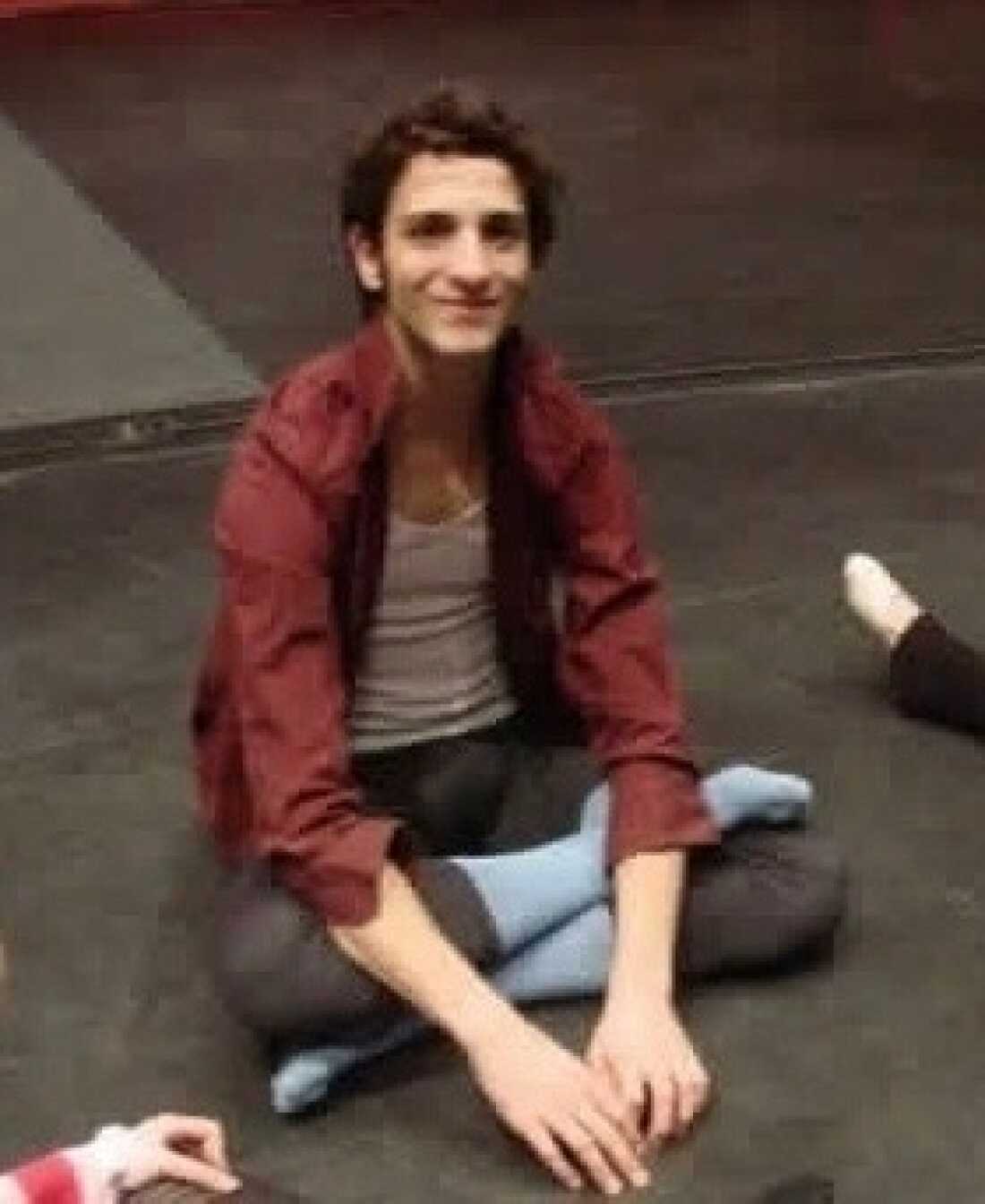 Paul Busch sits crossed legged on the floor wearing dance clothes.