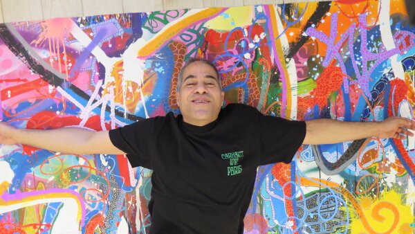 A man lies across a colorful graffiti-style painting with his arms outstretched.