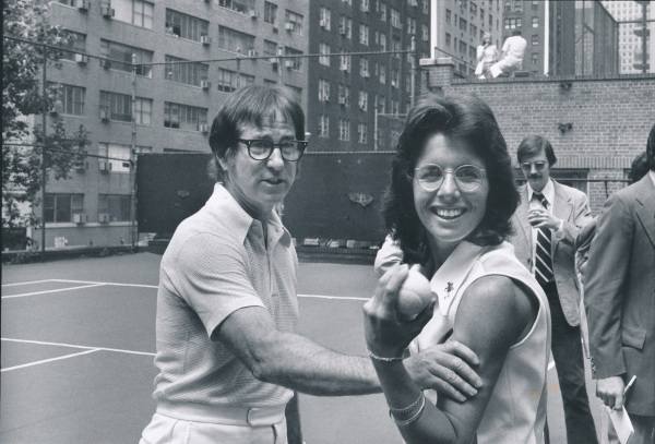 In this black-and-white photo, Billie Jean King stands with Bobby Riggs on a tennis court at a press event for the 1973 "Battle of the Sexes."