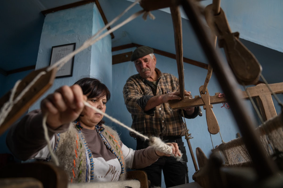Lubov Hychka demonstrates how to weave the hunia fabric while Vasyl Hychka (unrelated), who takes care of the property where the loom is housed, helps with the rickety old machine.