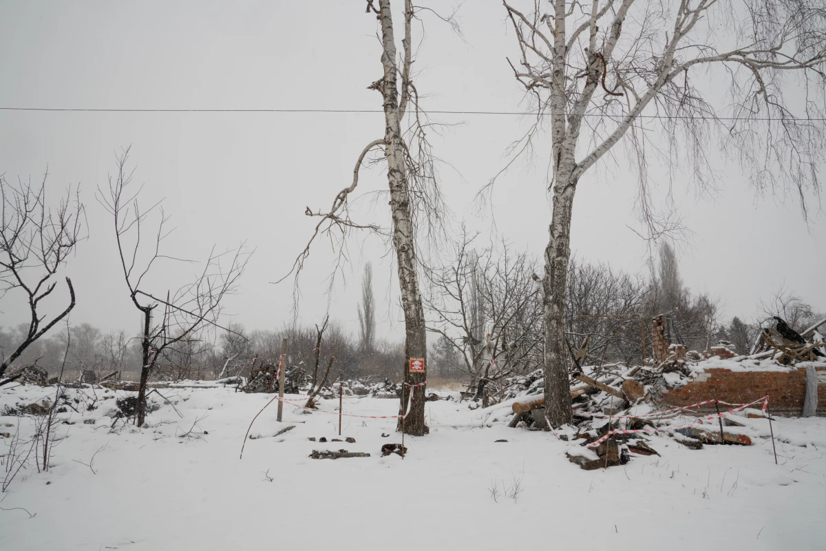 Destroyed homes in Staryi Saltiv are blanketed with snow in February. A sign warns of landmines and tape marks pieces of possibly unexploded ordnance on the ground.