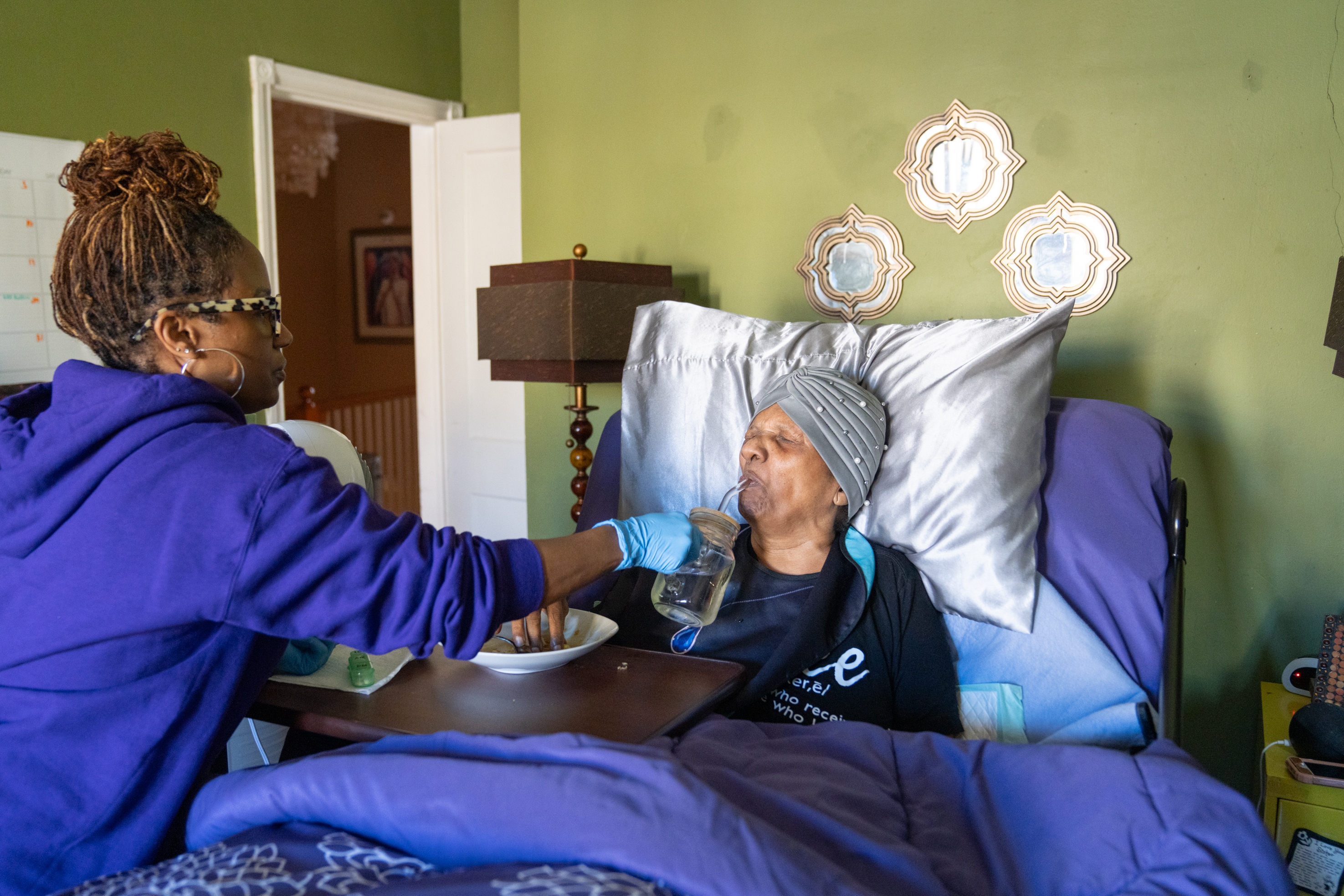Dawnita Brown gives her mother, Joan Cain, water to help swallow pills after breakfast. Brown is the primary caregiver to her mother and father, who live with her in Baltimore.