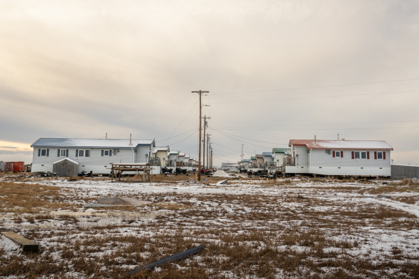 This photo shows two rows of small, one-story homes, one the right and the other on the left. A power line supported by poles runs down the aisle between the two rows.