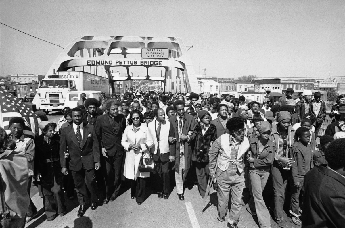 Aided by Father James Robinson, Mrs. Coretta Scott King, widow of Dr. Martin Luther King, Jr., center, and John Lewis, a crowd estimated by police at 5,000, marched across the Edmund Pettus Bridge from Selma, Ala. March 8, 1975.