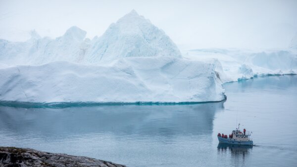 A large iceberg in Ilulissat, Greenland. On the water that surrounds the iceberg, a small boat is seen. 