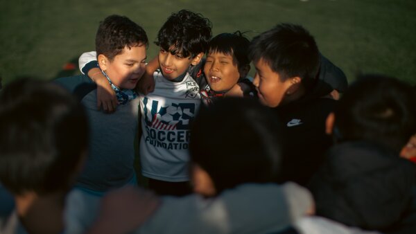 Children huddle during soccer practice. The faces of four young boys can be viewed.