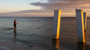 A person fishes next to a broken pier.