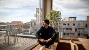 Sebastian Schublach sits next to the windows of his buildings shared kitchen and hosting space. Schublach has lived in this climate-friendly affordable apartment in Vienna for six years with his wife and two kids. At top: Schlubach sits in the building’s light filled rooftop kitchen and dining room.