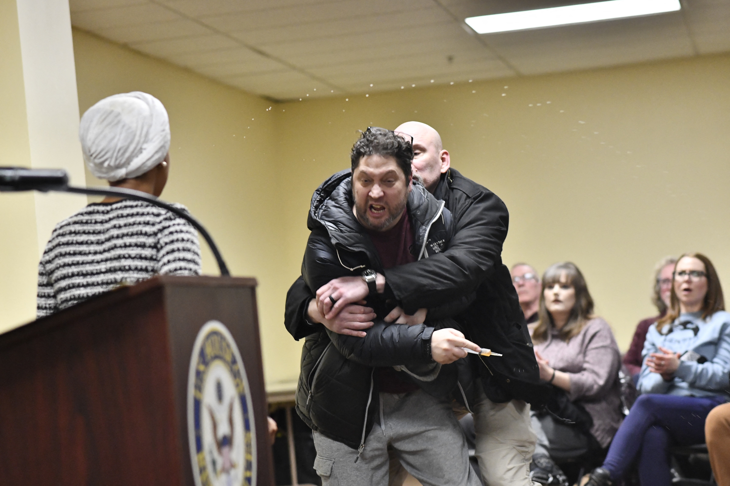 A man is tackled after spraying an unknown substance at US Representative Ilhan Omar (D-MN) (L) during a town hall she was hosting in Minneapolis, Minnesota, on January 27, 2026. (Photo by Octavio JONES / AFP via Getty Images)