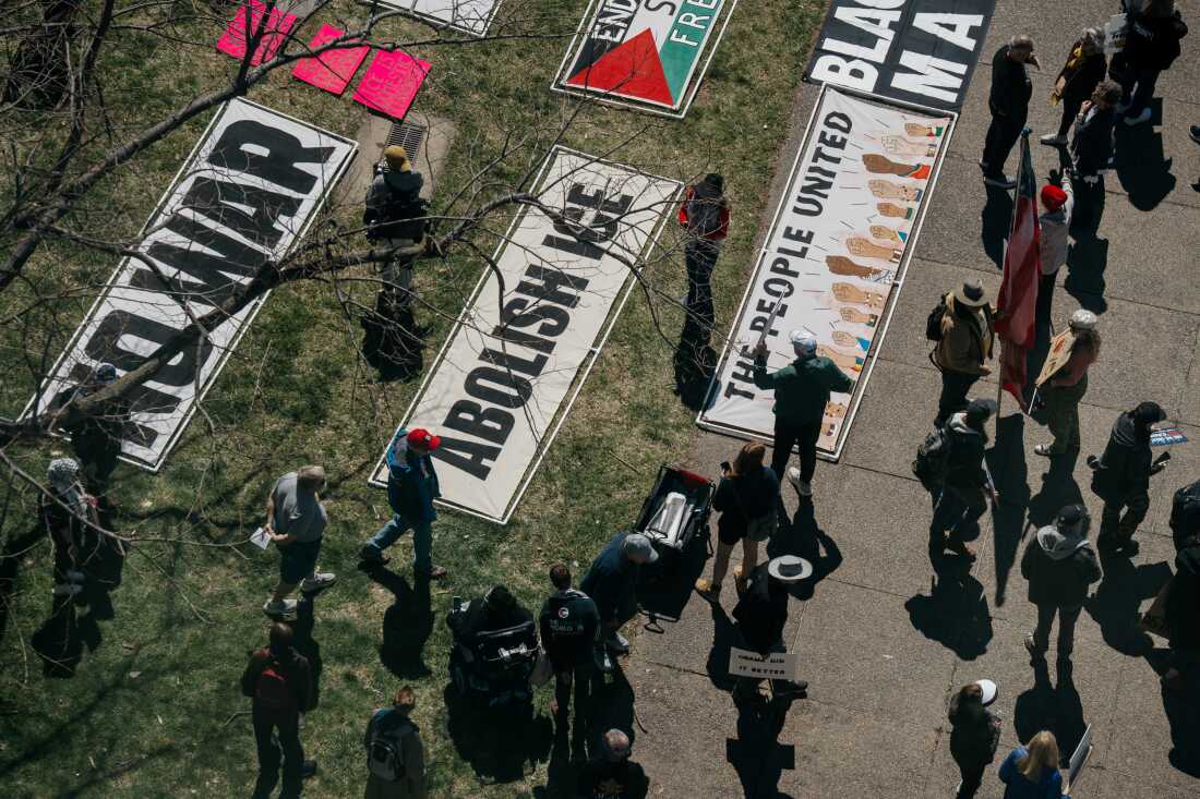 Demonstrators walk by large banners decrying the U.S. conflict in Iran and U.S. Immigration and Customs Enforcement during a “No Kings” protest on Saturday, March 28, 2026, in downtown St. Louis.