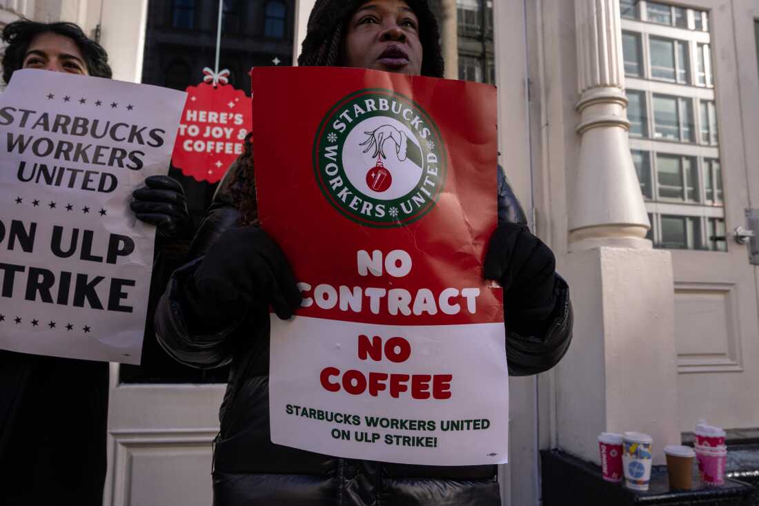 People hold signs outside of a closed Starbucks as employees strike on Monday in New York City.