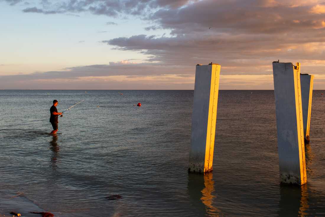 A person fishes next to a broken pier in Fort Myers Beach, Fla., in October. The city is still rebuilding after Hurricane Ian devastated the area in 2022. High costs for construction and insurance have made Fort Myers Beach unaffordable for many who called it home before.