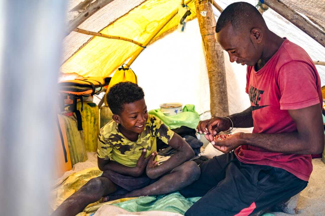 Migrant Vezo fisherman Netson Kassim, 30, shares peanuts with his son in the tent they live in for 9 months a year.