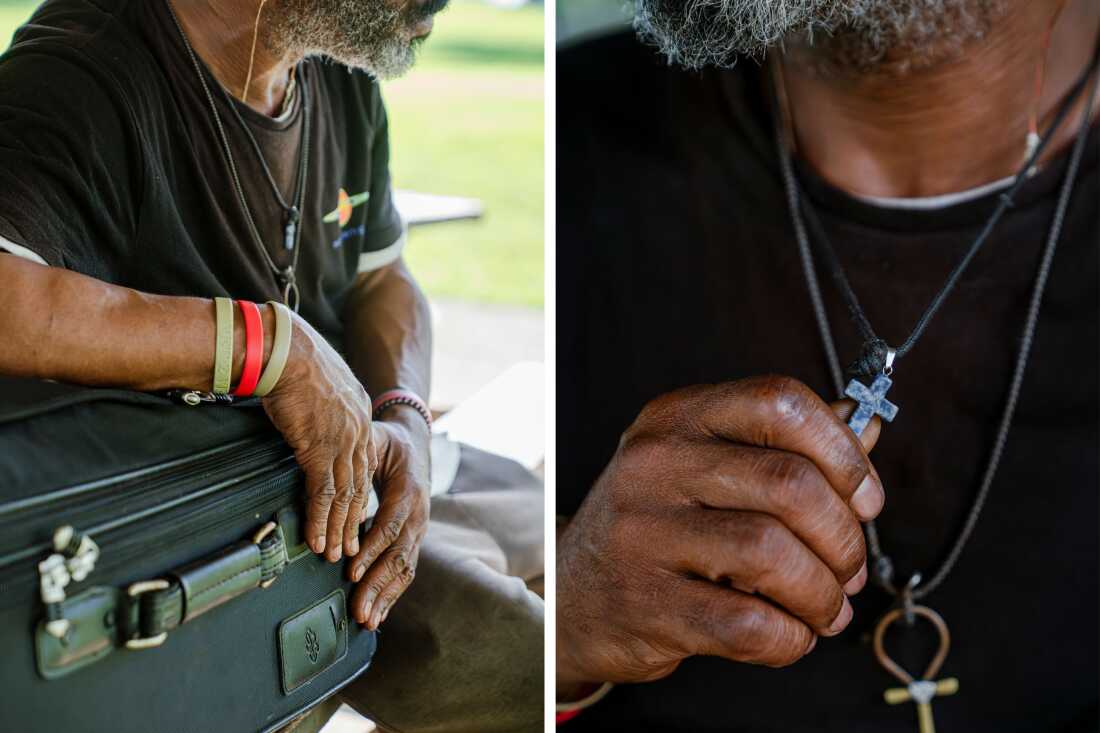 Joseph Williams holds a cross and rests his arm on top of his suitcase under the pavilion where he sleeps.