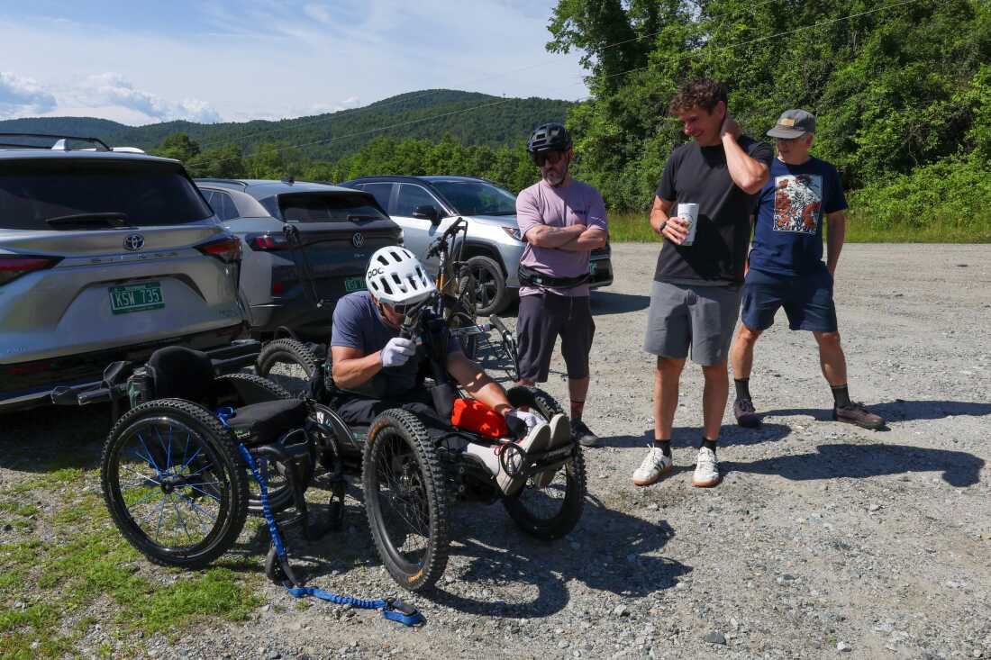 Louis Arevalo, left, straps into his adaptive mountain bike and chats with Jeff Dickson of the Vermont Mountain Bike Association, Angus McCusker with Vermont Huts and Trails, and volunteer Thatcher Hinman (all from left) ahead of a trail accessibility assessment in Randolph, Vermont, on Thursday, June 25, 2026.