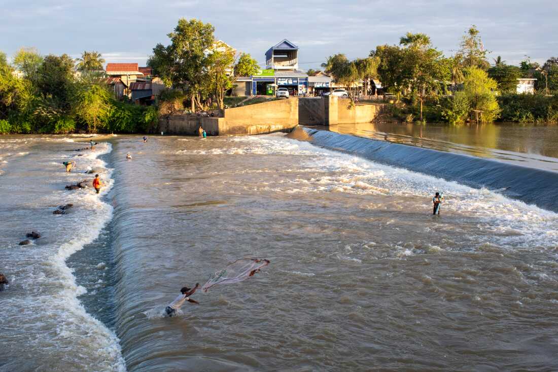 As afternoon clouds recede, fishermen use nets to catch fish in the shallow Pursat River.
