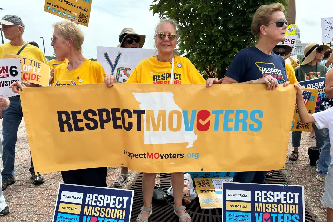 Three people stand outside behind a banner that says RespectMOVoters.
