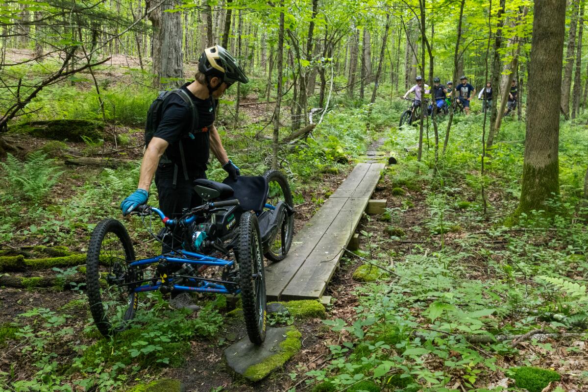 Nick Bennette, of the Vermont Mountain Biking Association, guides an adaptive bike over a narrow bridge, pointing out that other adaptive riders may have trouble getting across.