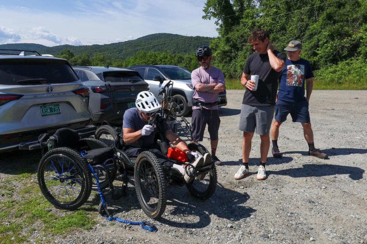 Louis Arevalo, left, straps into his adaptive mountain bike and chats with Jeff Dickson of the Vermont Mountain Bike Association, Angus McCusker with Vermont Huts and Trails, and volunteer Thatcher Hinman (all from left) ahead of a trail accessibility assessment in Randolph, Vermont, on Thursday, June 25, 2026.