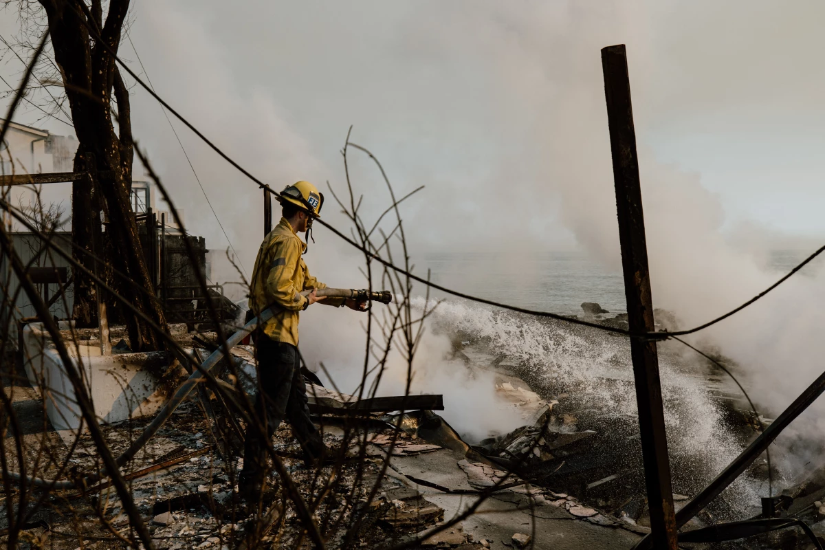 A firefighter works with water hoses near houses burned down in the Palisades Fire along the Pacific Coast Highway in Malibu, Calif. on Jan. 9, 2025.