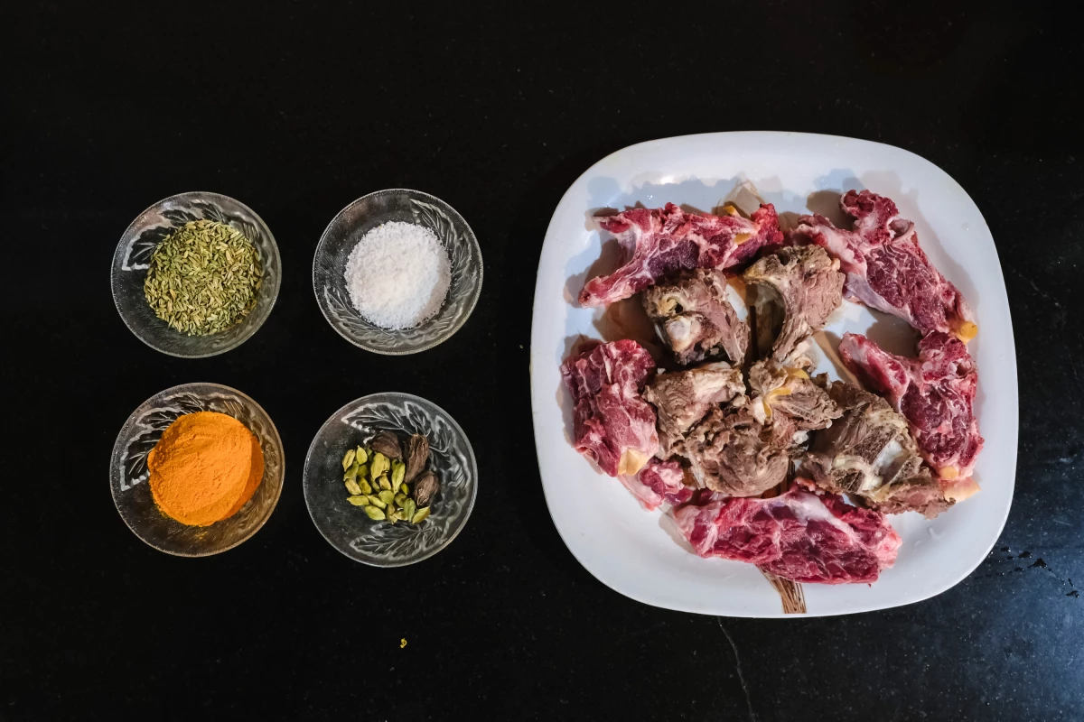Left: A tray holds the key ingredients — goat meat, fennel seeds and mild spices. Simple and nourishing, these ingredients come together to make the comforting Kashmiri mutton soup. Right: Arsha Begum lifts a piece of tender goat meat from the golden broth — finally ready to eat. It's warm, nourishing and full of tradition, just as it has been for generations.