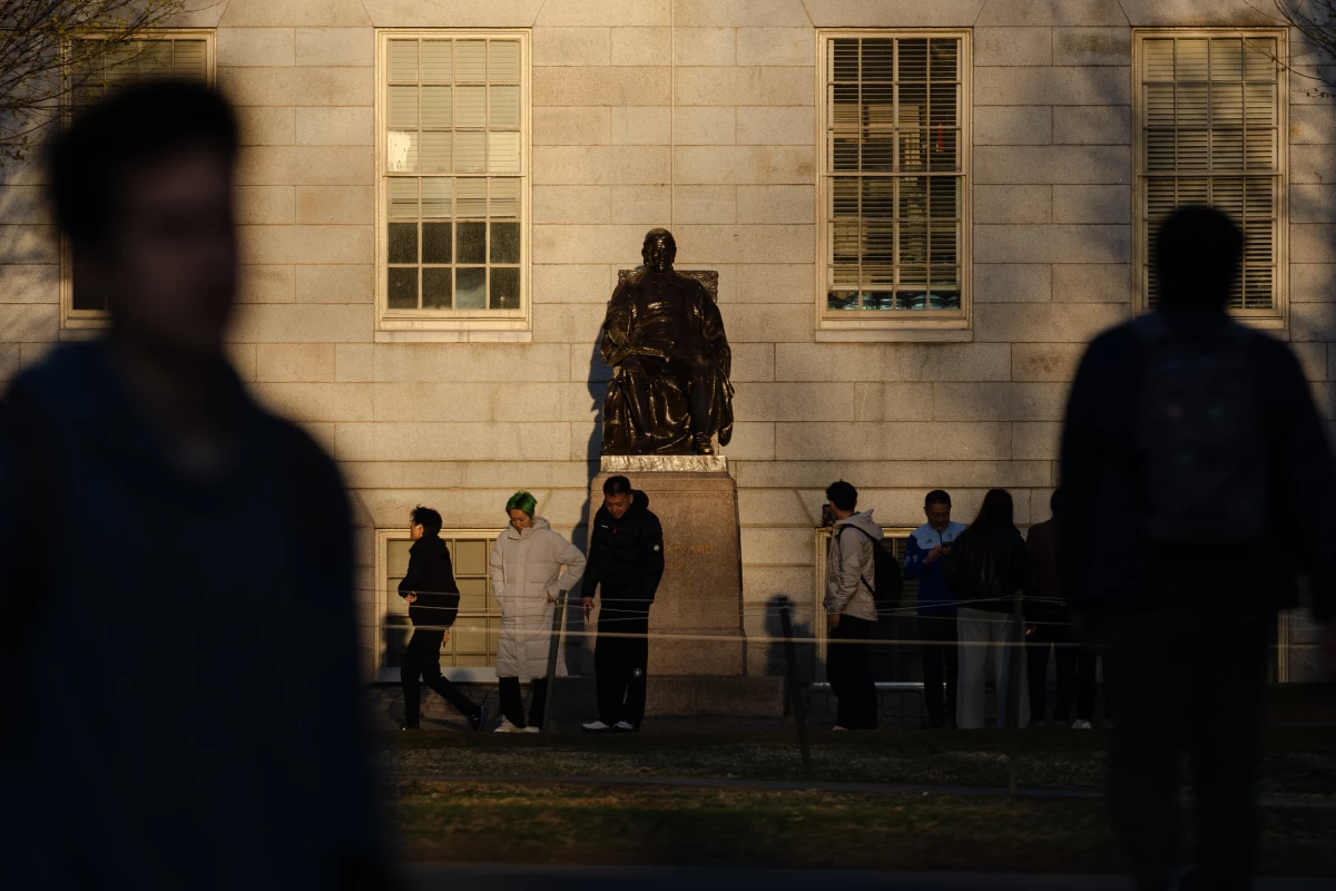 People gather to take photos with the John Harvard statue at Harvard University. President Trump made another threat to Harvard's tax-exempt status in a social media post on Friday.