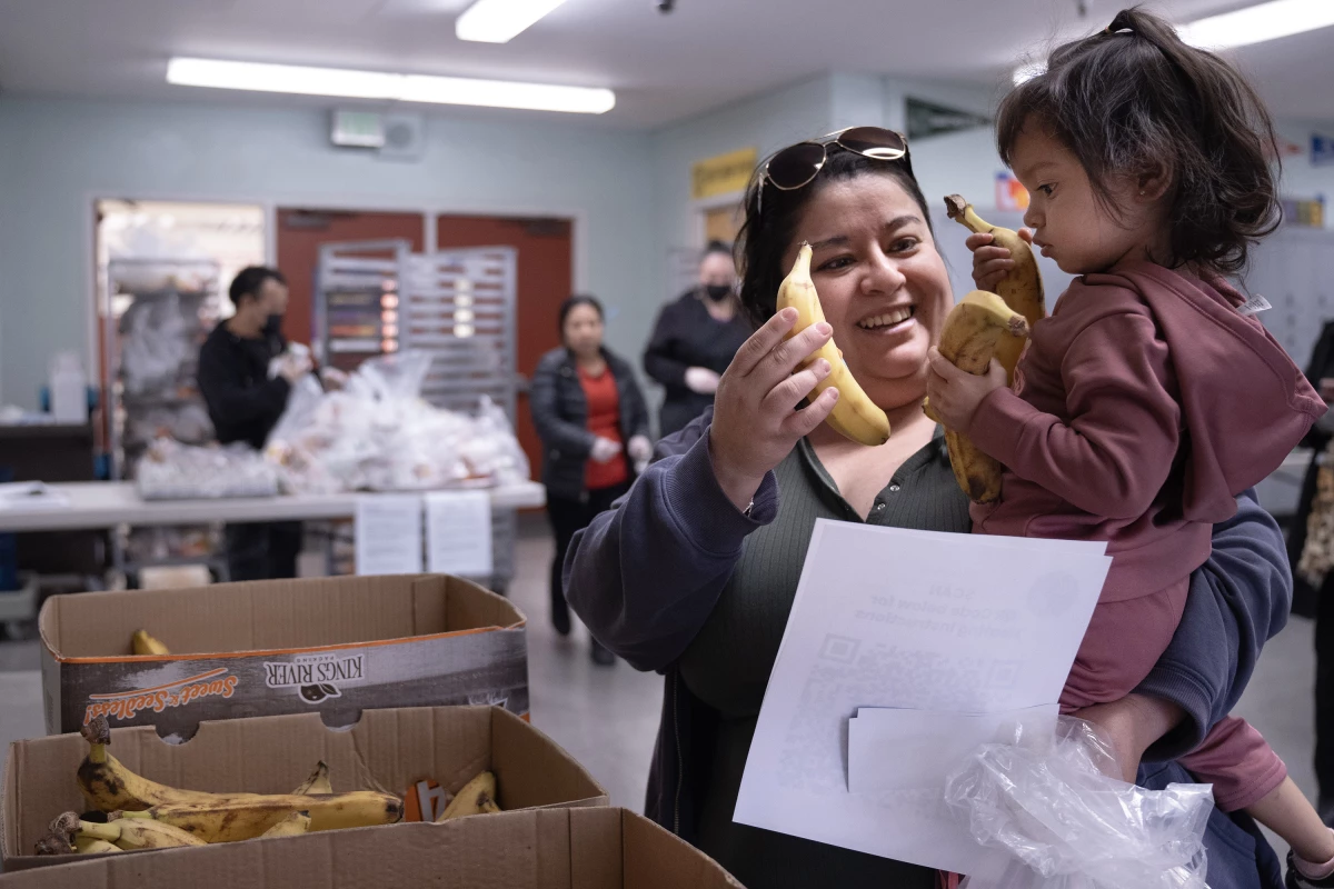 Rocio Manzo and her 1-year-old daughter, Jaliy, grab some bananas at Hollenbeck Middle School on Friday, Jan. 10. Hollenbeck has become a designated grab-and-go meal location for LAUSD students, along with 15 other sites across the district.