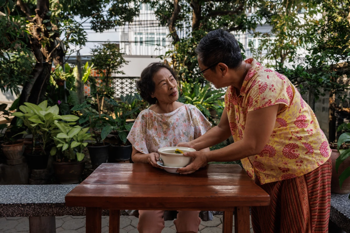 Hnoi Lathitham (right) serves a bowl of gang liang to her aunt, Ankachatra Janpiban, at their home in Bangkok.