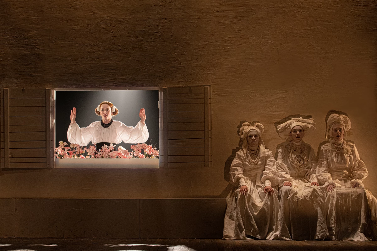 A scene from a Ukrainian production of The Witch of Konotop. At the window, Olena, played by Mariia Rudynska, is the love interest of the main character but does not love him back. And a three-witch chorus is seen right.