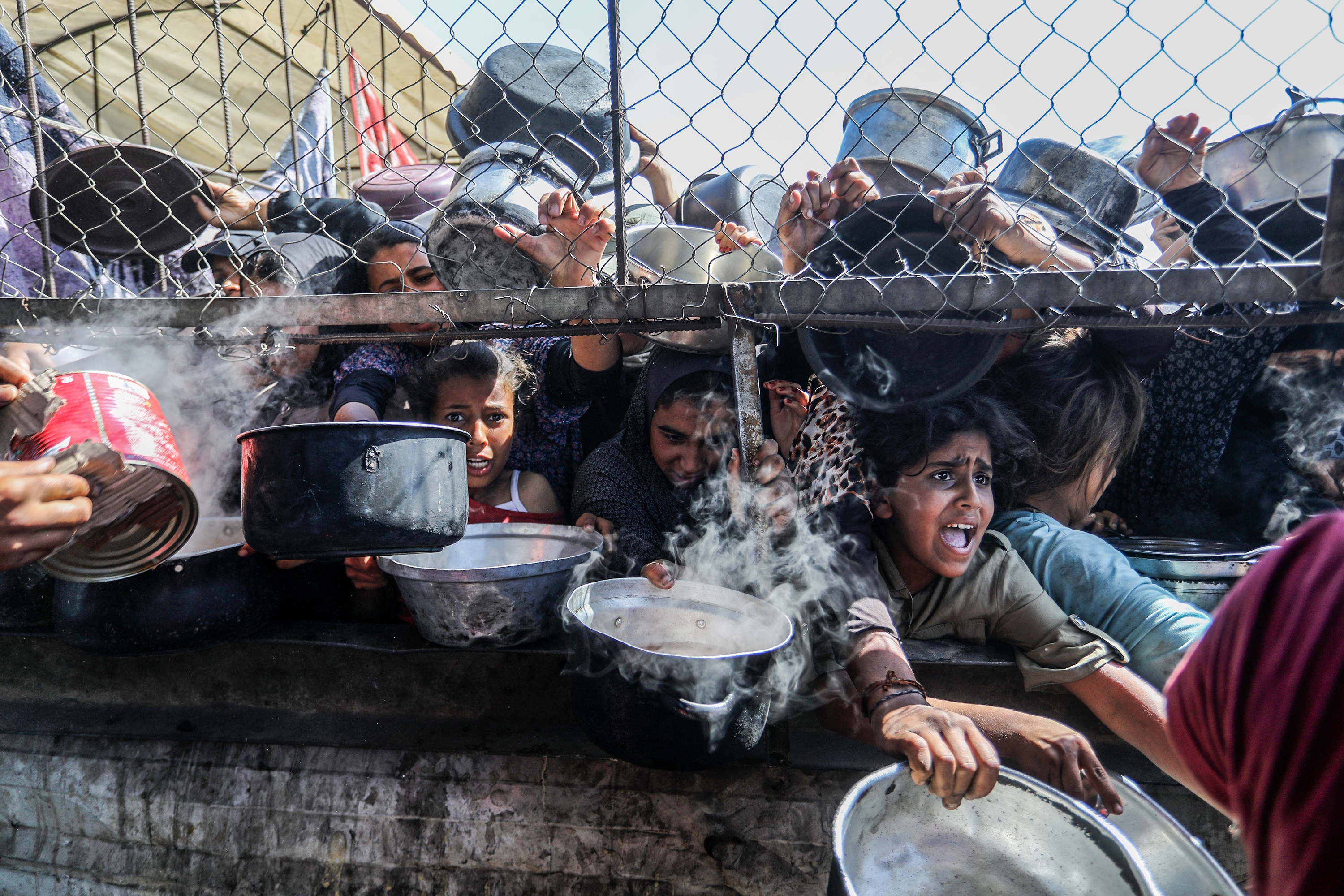 Displaced Palestinians, including women and children living in tents, receive food distributed by aid organizations in al-Mawasi district of Khan Younis, Gaza, on May 30. In Jordan, tens of thousands of boxes of food aid for Gaza are moldering in warehouses.