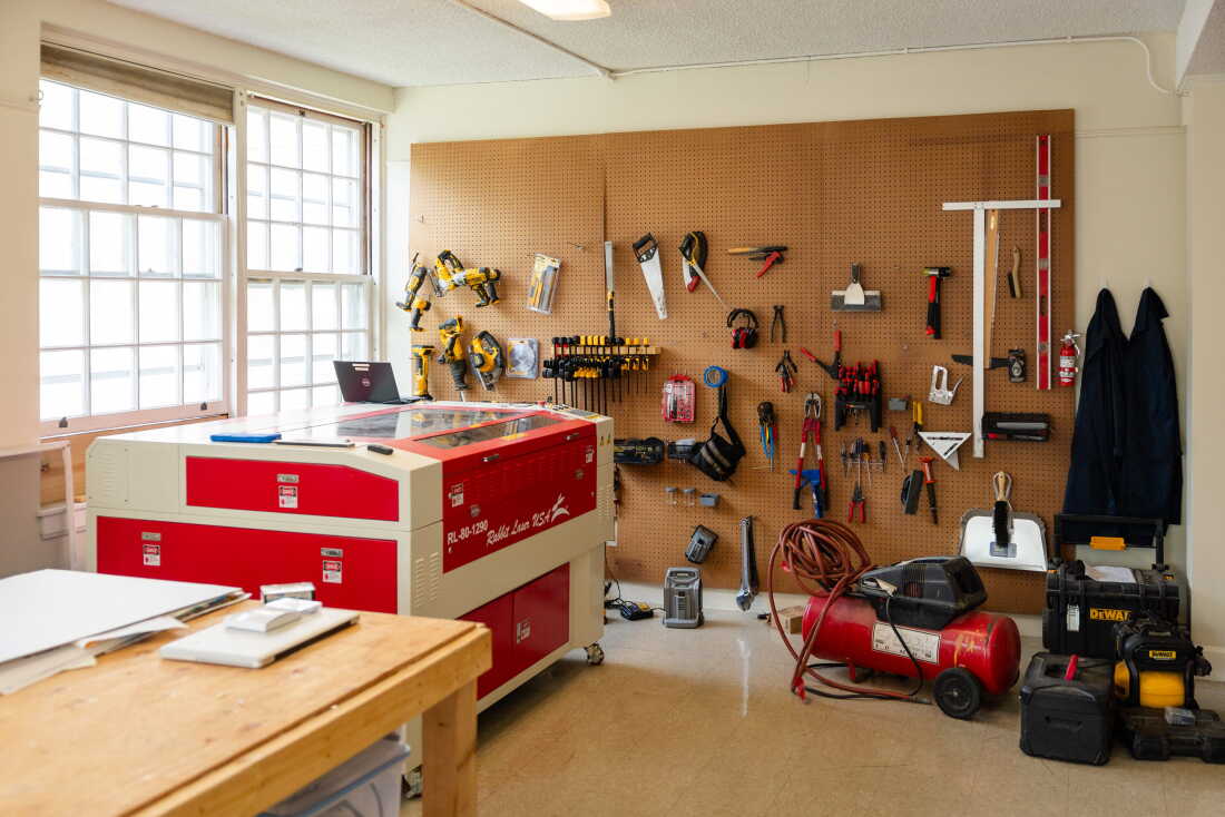 This photo shows part of a shop room at the Greenway Institute. Tools hang from a large pegboard that covers one wall. The room also has a wooden worktable and various pieces of equipment.