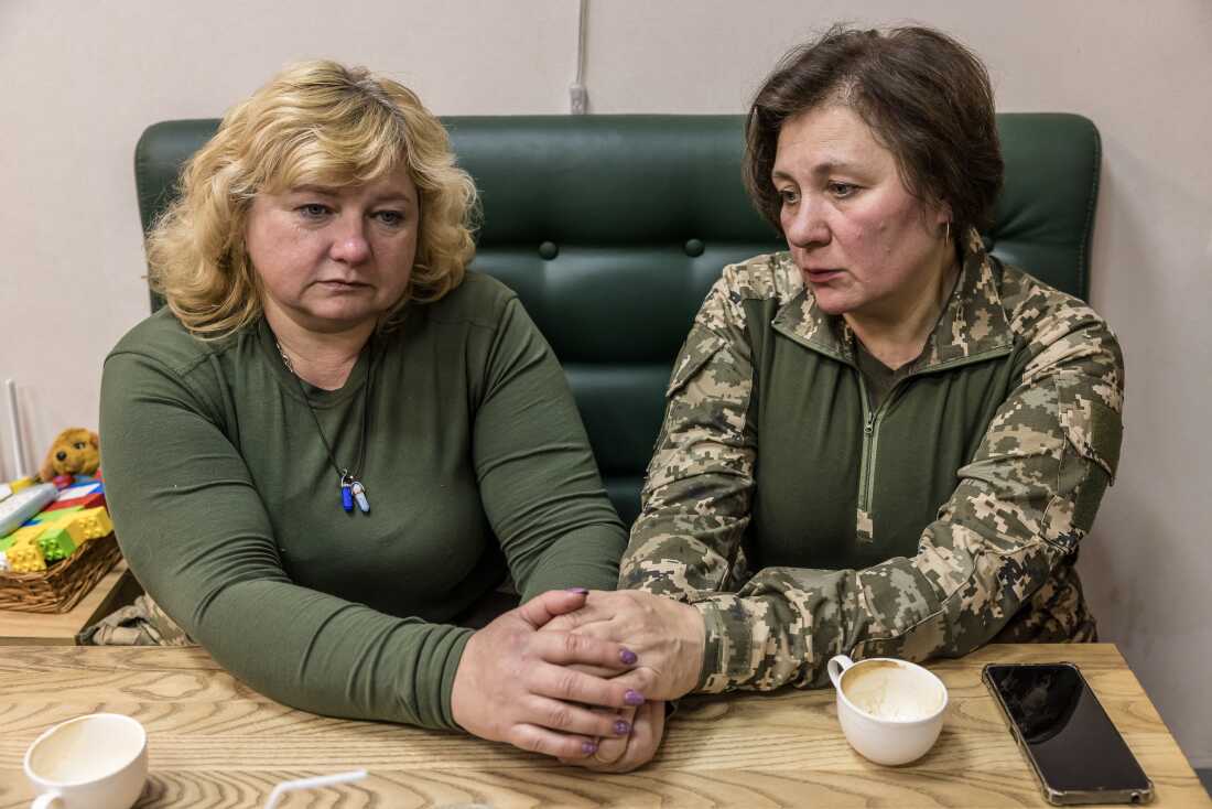 Two women hold hands while seated at a table in a coffee shop.