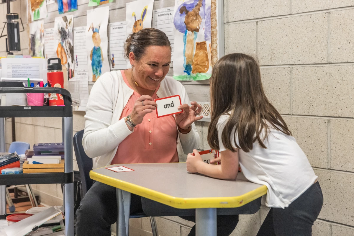 Teaching assistant Nicki Longyear works one-on-one with a kindergartener in the hallway outside a classroom at Mill Stream Elementary School.