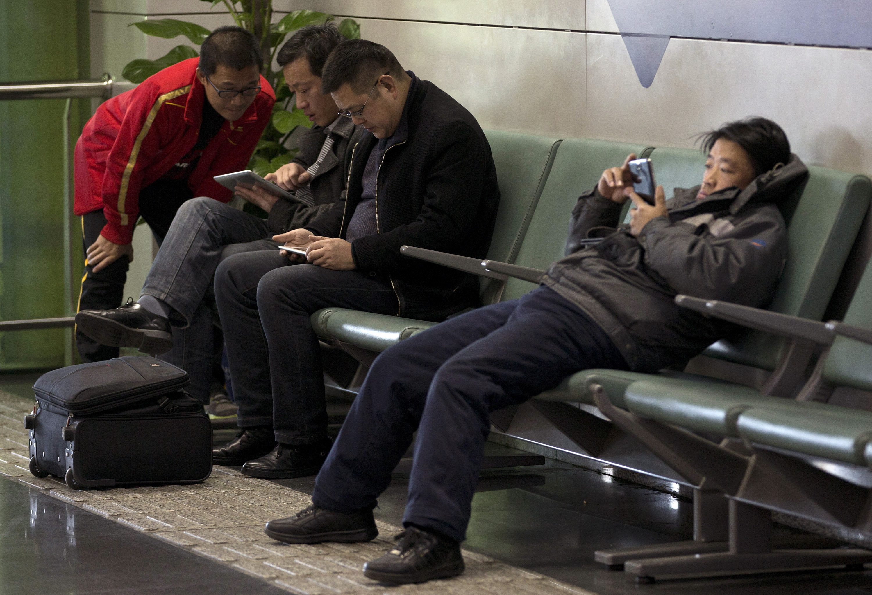 Men browse their tablet computers and smartphone at the Beijing Capital Airport on Nov. 30, 2013.