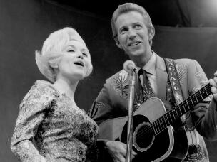 Country singer Dolly Parton and her collaborator Porter Wagoner perform onstage in circa 1967. Mr. Wagoner is wearing a Nudie Suit designed by Nudie Cohn of Nudie's Rodeo Tailors.