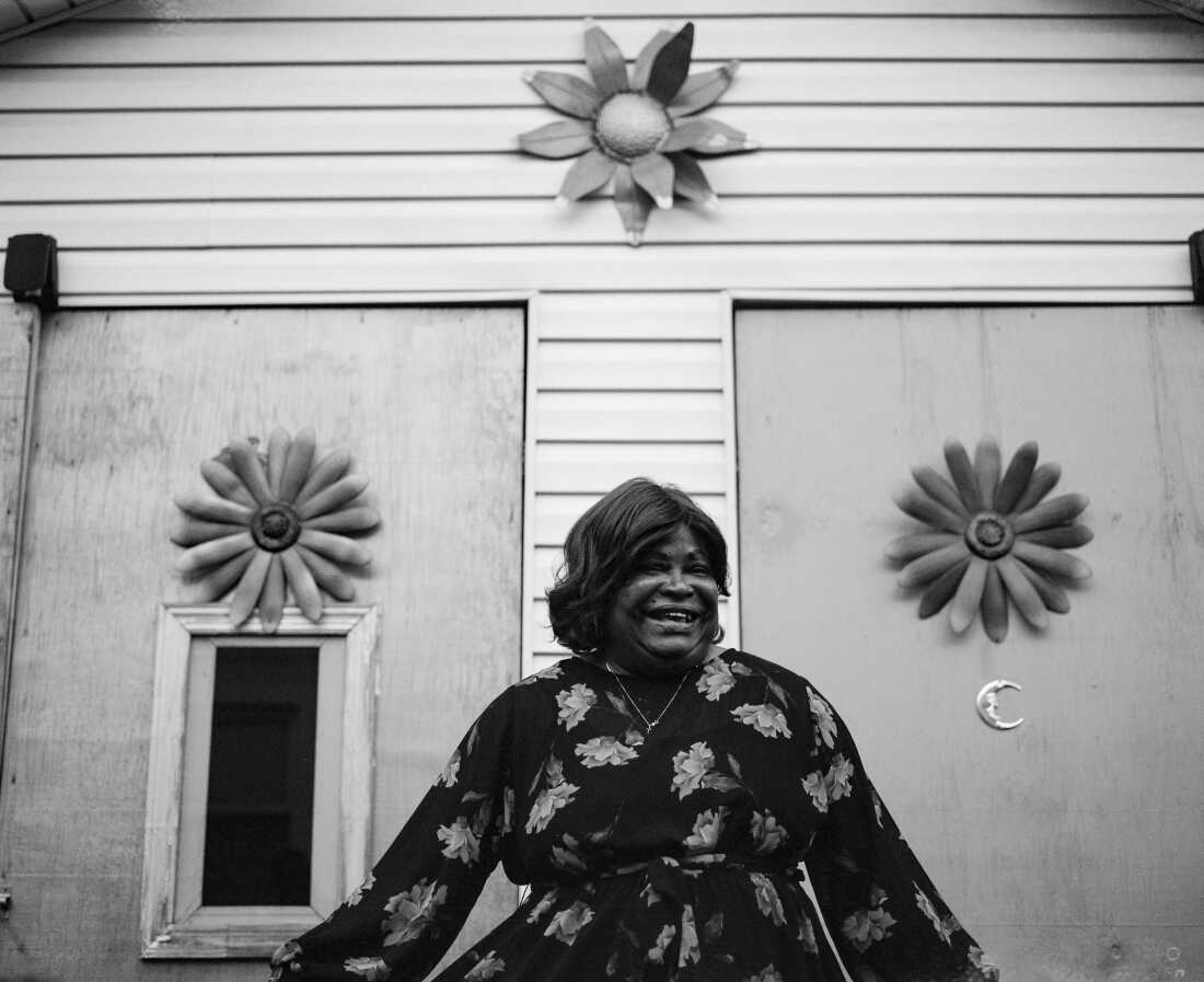 Stevens’ grandmother Lillie Coleman, 71, holds a floral dress in front of a shed decorated in flowers outside her home in Cambria Heights.