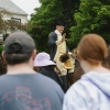A reenactor dressed as George Washington, wearing a tricorn hat, waves to the crowd from atop his horse.