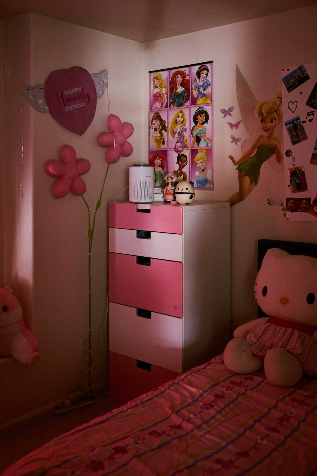 A sliver of light shows a bedroom with a pink dresser, a poster of Disney princesses and Tinkerbell on the wall. There is a large Hello Kitty stuffed animal on a pink bedspread.