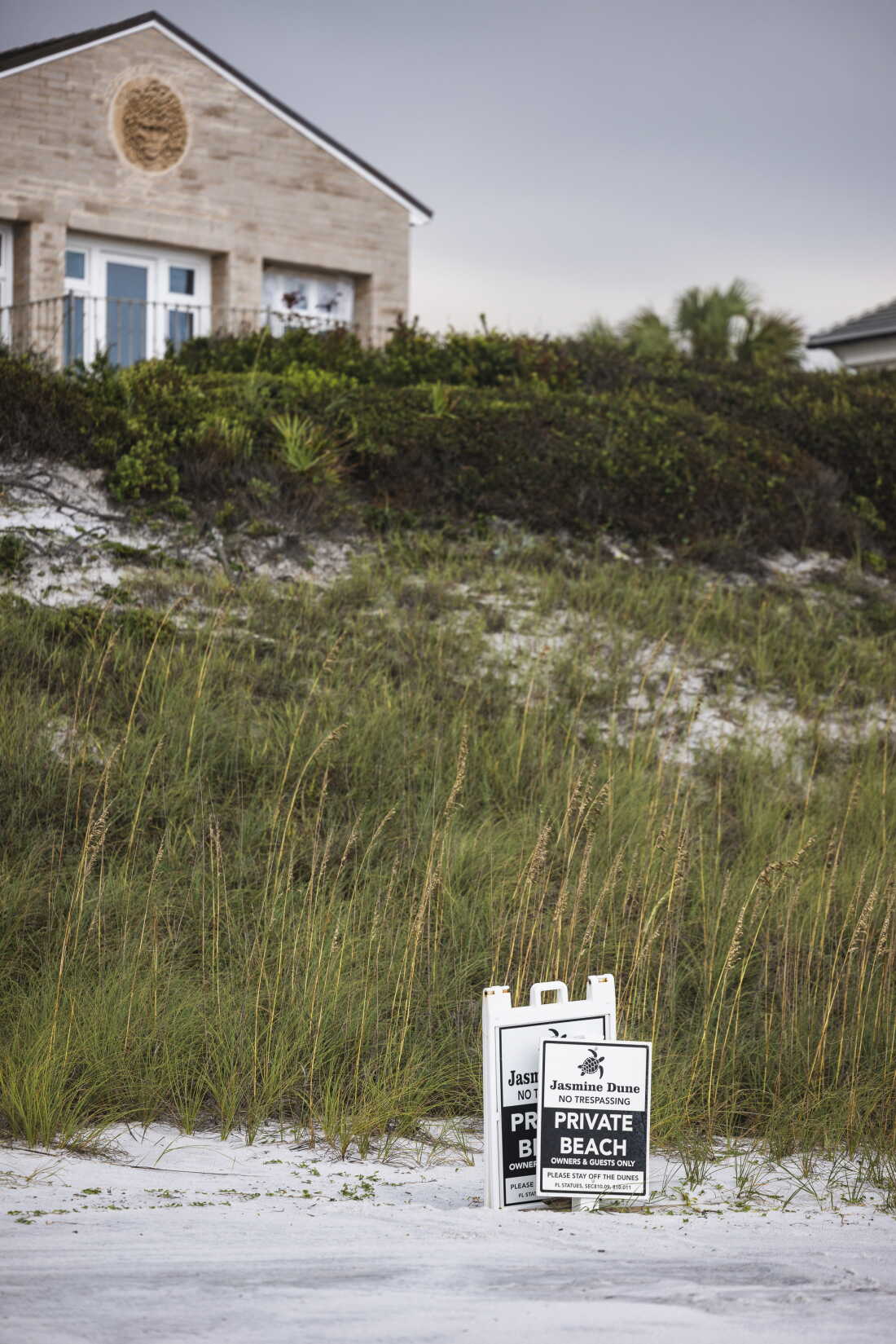 Two signs saying "NO TRESPASSING," "PRIVATE BEACH" and "OWNERS & GUESTS ONLY" stand on the white sand at Dune Allen Beach in Florida on August 20. A dune slopes upward behind the signs, leading up to the back of a residence.